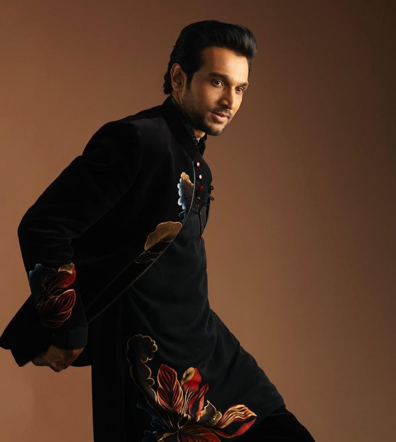 Pratik Gandhi brings a classy vibe to the party in this black velvet plain kurta featuring red and orange floral designs near the buttons, with a full-sleeved jacket in the same pattern, plain black pants, and polished black shoes.